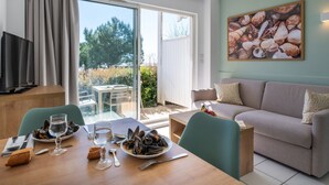 A dining area with a table set for two, a sofa, and a television. - Résidence Odalys Les Terrasses de Fort Boyard (Fouras)