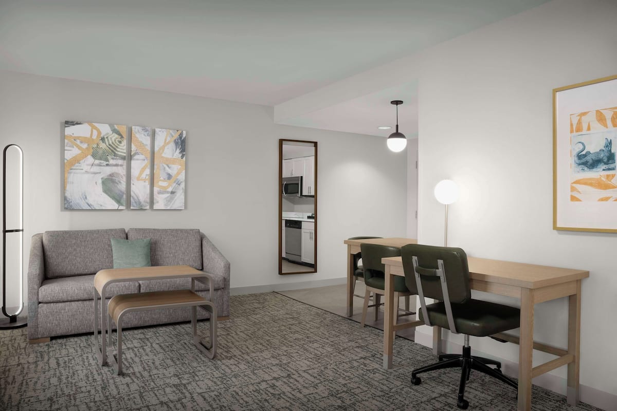 Une pièce moderne avec un canapé gris, un bureau en bois et une chaise verte. Un miroir est accroché au mur et un tableau se trouve au-dessus du bureau.