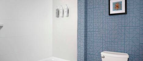 Baño con tina blanca, inodoro y zona de ducha. Hay tres botellas en la pared.