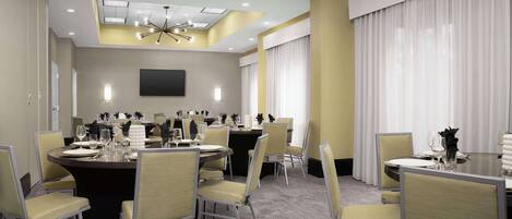A conference room with round tables, chairs, a flat-screen TV, and a ceiling light fixture.