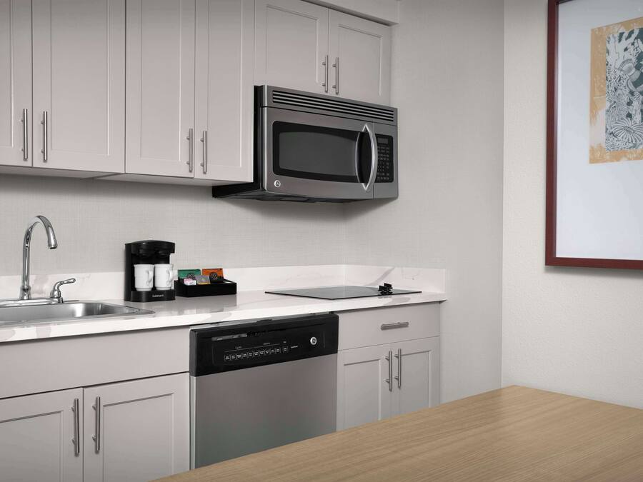 A modern kitchen with white cabinetry, a stainless steel microwave, a coffee maker, and a dishwasher.