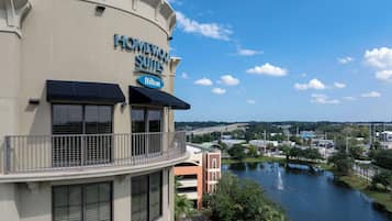 Ein Hotel namens Homewood Suites mit einem Hilton-Logo, einem Balkon mit Geländer und Blick auf einen Fluss sowie umliegende Grünflächen.