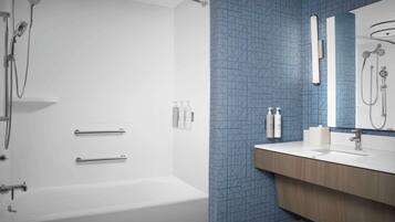 Une salle de bain avec une baignoire blanche, une douche équipée d’un pommeau de douche amovible et un meuble-lavabo avec un miroir.