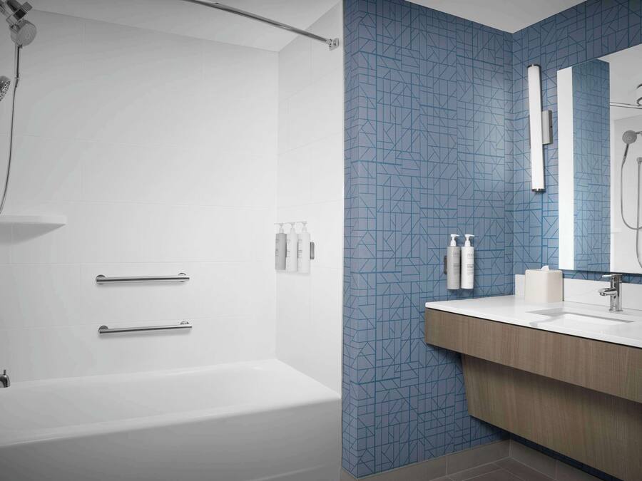 Une salle de bain avec une baignoire blanche, une douche équipée d’un pommeau de douche amovible et un meuble-lavabo avec un miroir.