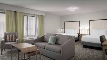 Habitación de hotel con sofá, sillón, dos camas, una mesita y una ventana con cortinas.