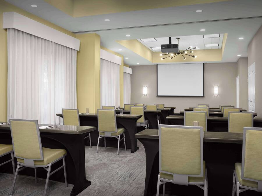 A conference room with multiple tables and chairs, a projector screen, and a ceiling light fixture.