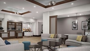 A modern hotel lobby with a reception desk, seating area, and a kitchen in the background. - Homewood Suites by Hilton Jacksonville Downtown-Southbank (Jacksonville)