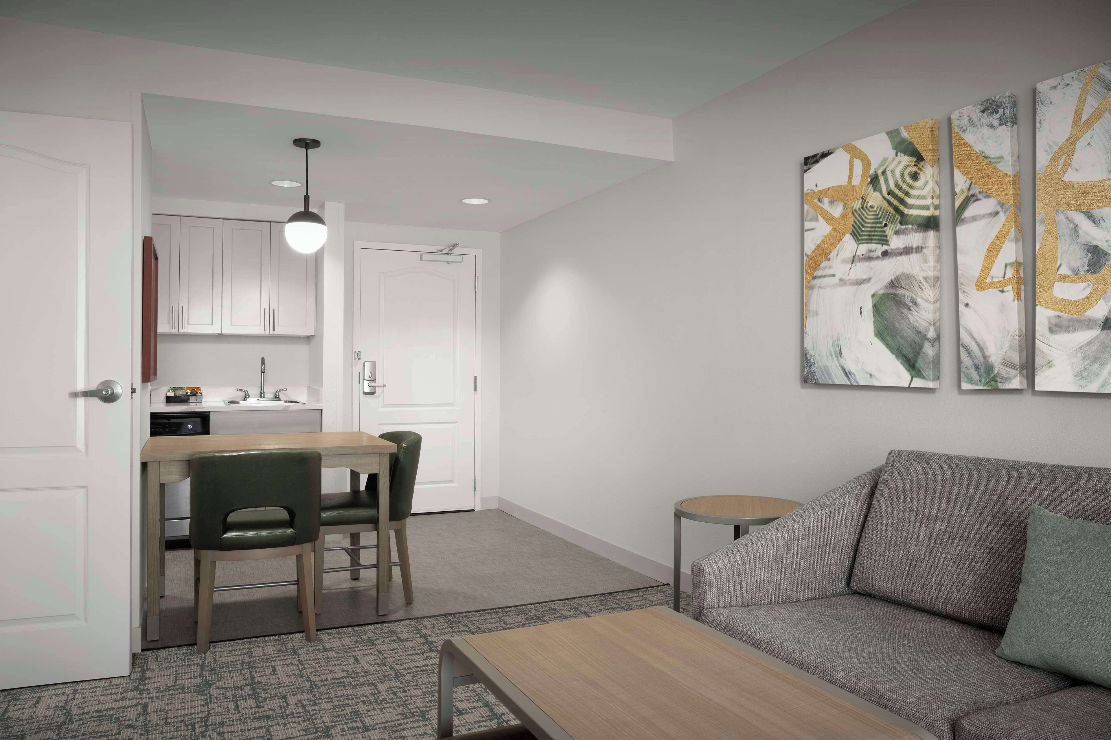 A modern living room with a grey sofa, a wooden coffee table, and a dining area with a table and chairs.