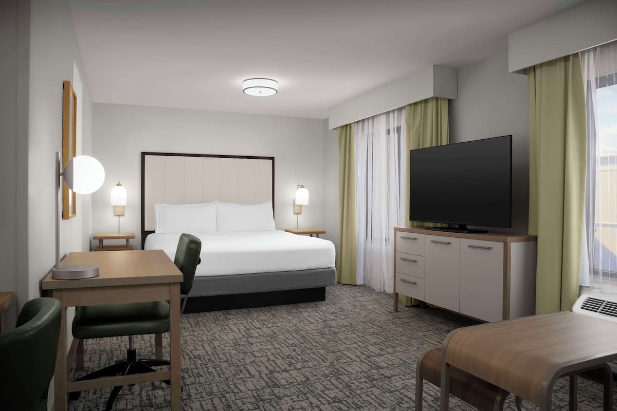 Une chambre d’hôtel comprenant un lit, un bureau, une chaise, une télévision et une commode.