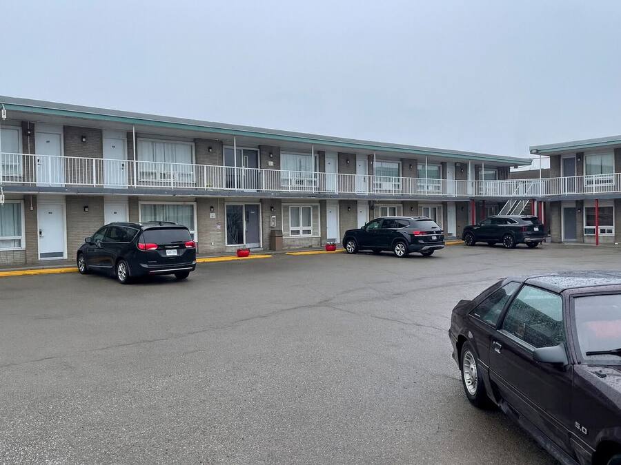 A motel with a row of rooms, each with a door and a window. There are cars parked in front of the motel.