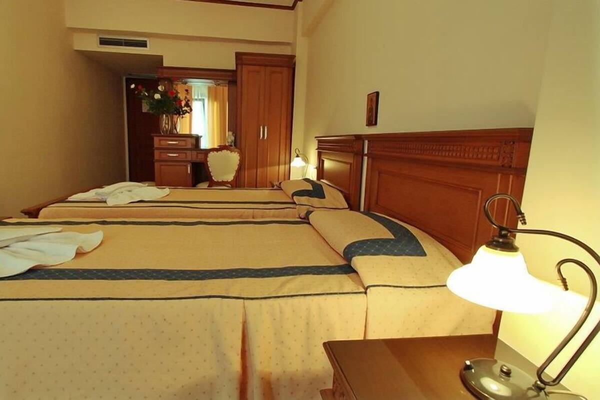 A hotel room with two beds, a wooden headboard, a bedside lamp, and a dresser with a mirror.