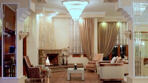 A spacious living room with a fireplace, leather armchairs, a sofa, and a chandelier. - Famissi Hotel (Kalabaka)