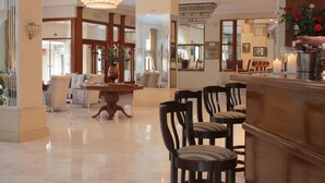 A hotel lobby with a chandelier, a reception desk, and a dining area with chairs and a table. - Famissi Hotel (Kalabaka)