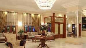 A spacious lobby with a chandelier, sofas, armchairs, and a coffee table with a floral centerpiece. - Famissi Hotel (Kalabaka)