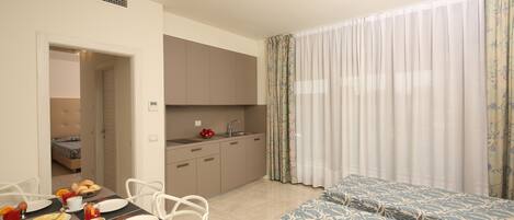 A hotel room with a dining area, kitchenette, and two beds.