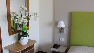 Une chambre d’hôtel avec un lit, une table de chevet avec une lampe, un téléphone, un miroir et une plante posée sur une commode.