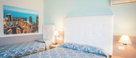 A hotel room with two beds, a large painting of a coastal scene, and an air conditioning unit.