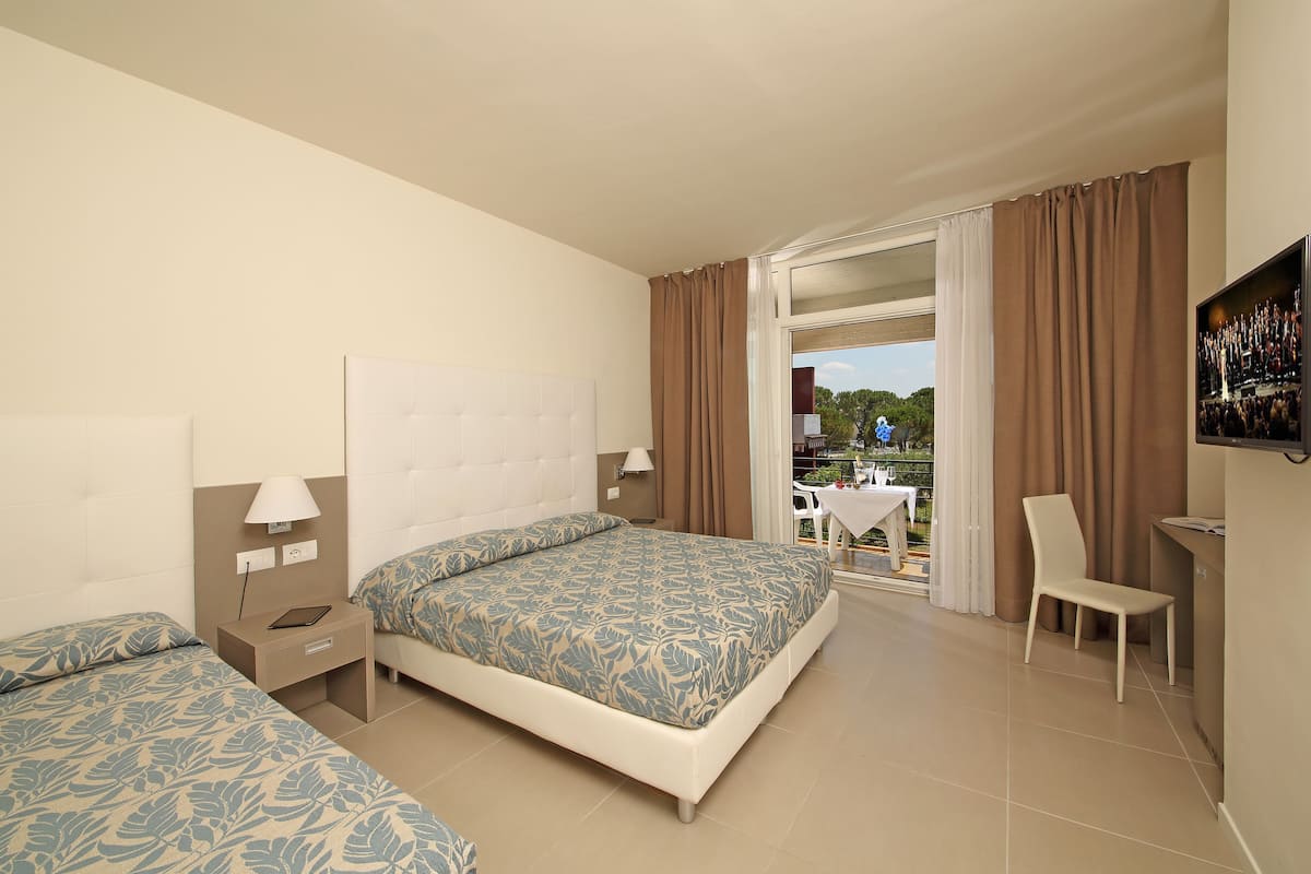 A hotel room with two beds, a TV, a desk, and a balcony with a table and chairs.
