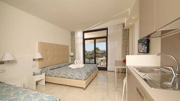 A hotel room with a bed, bedside table, lamp, and a view of the outdoors.
