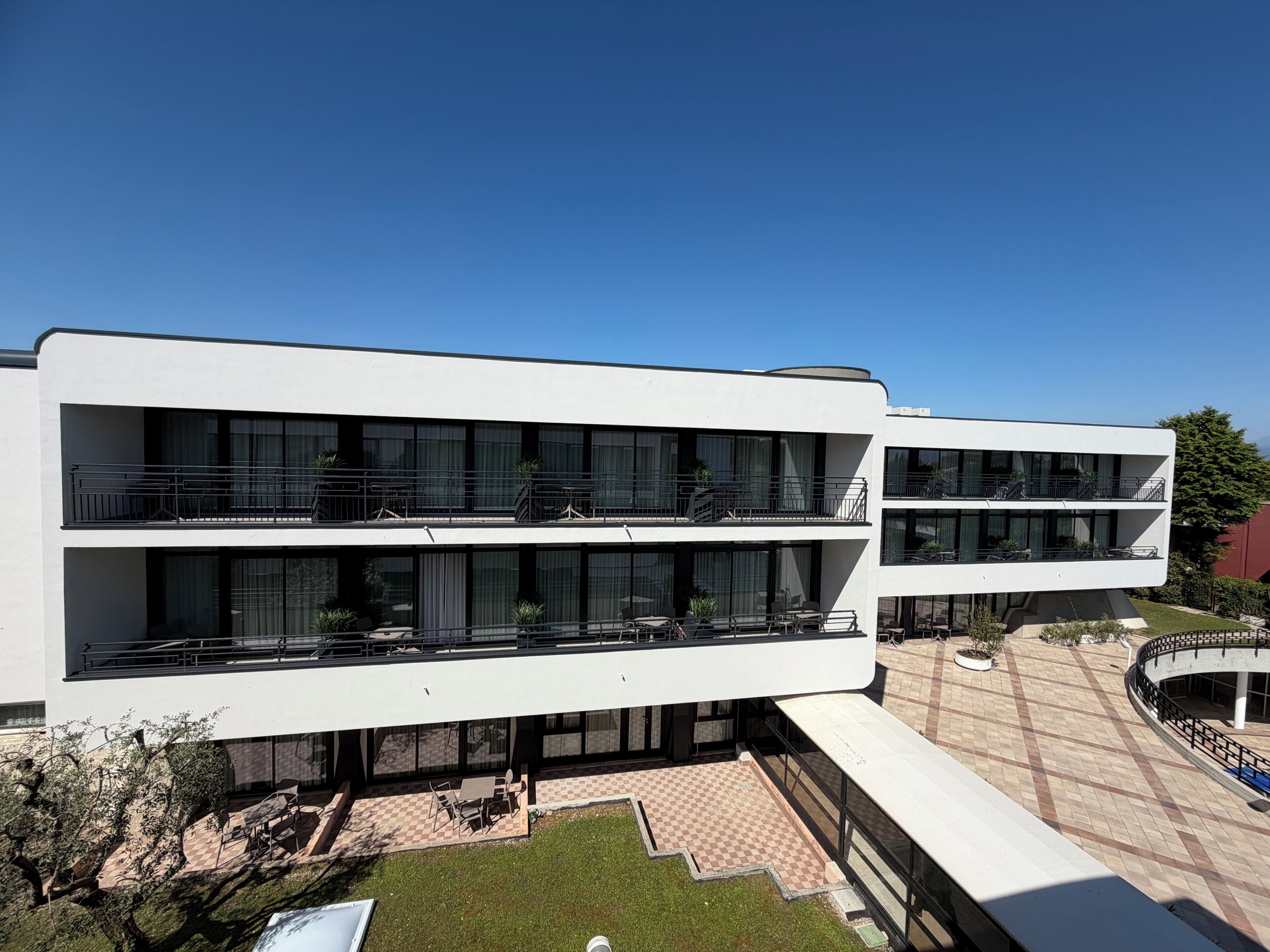 A modern multi-story building with balconies, outdoor seating, and a checkered pavement area.
