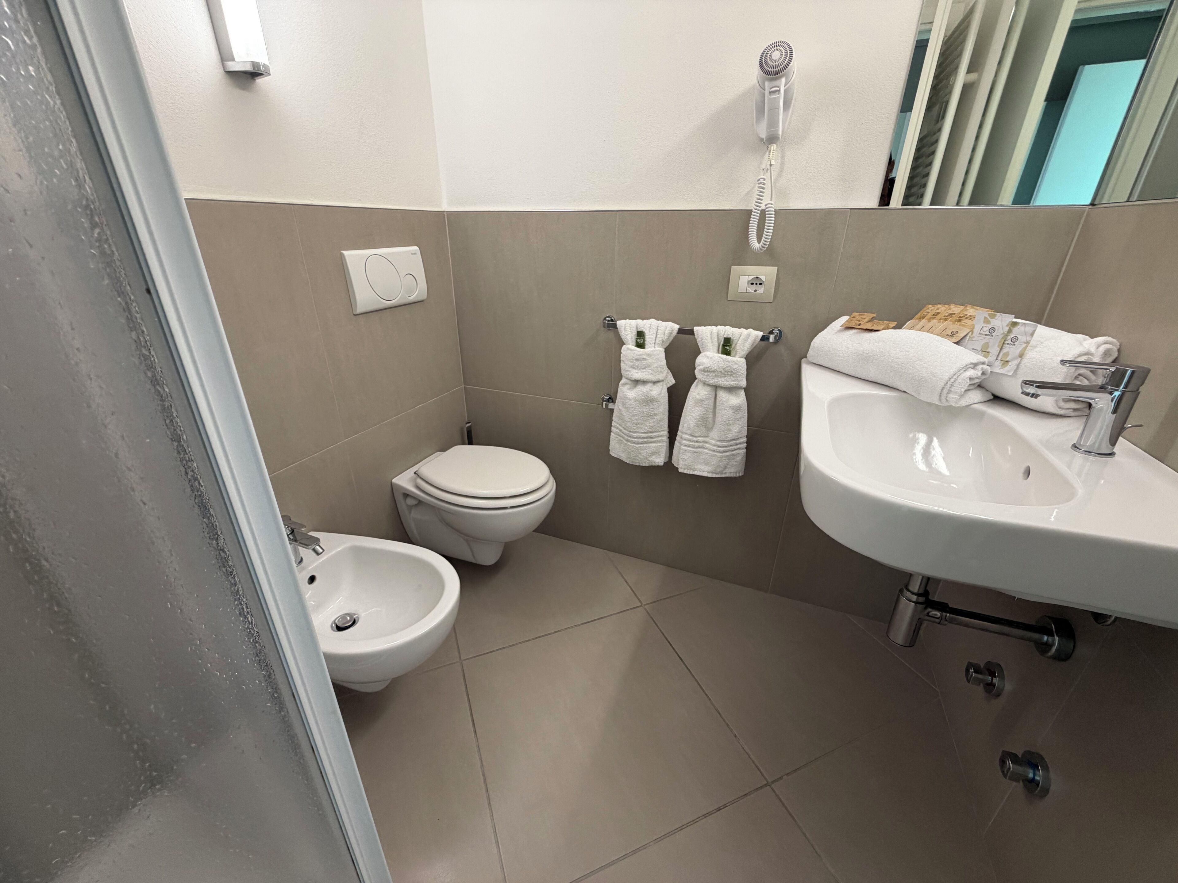 A compact bathroom with a toilet, bidet, sink, and towel rack.