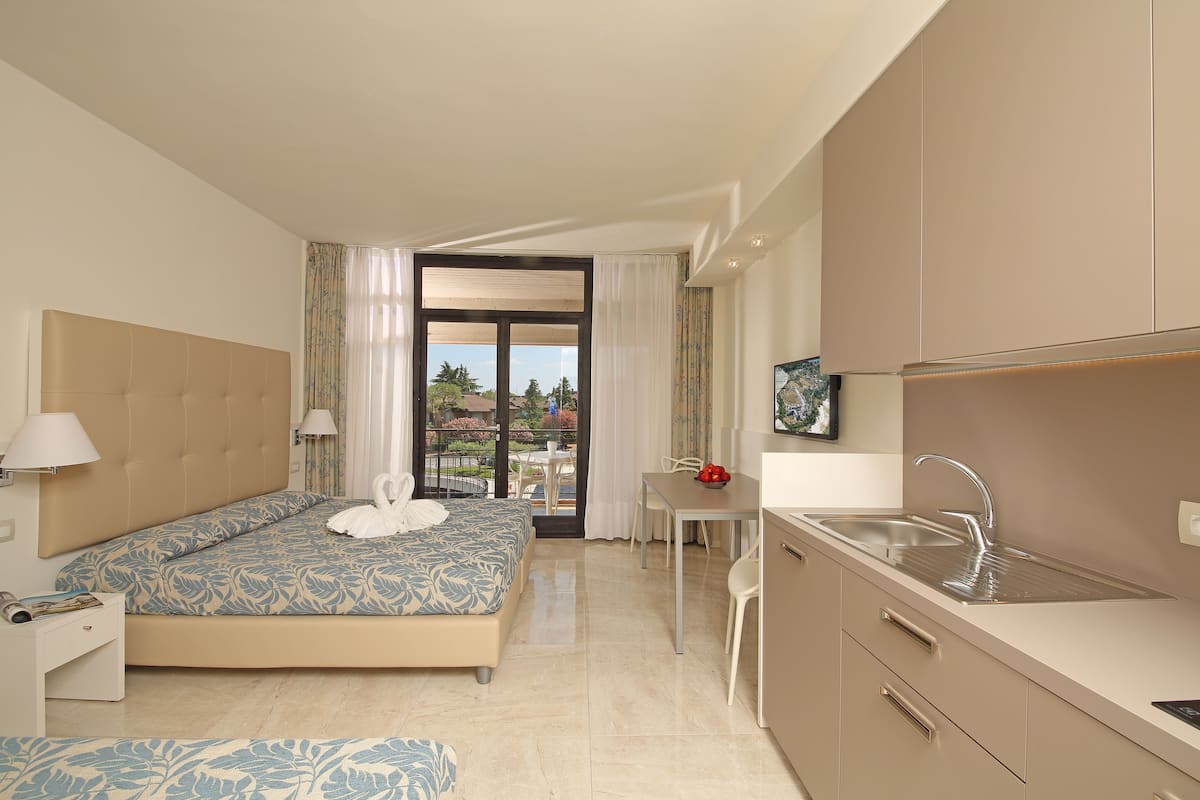 A hotel room with a bed, a dining table, a kitchen area, and a balcony with a view.