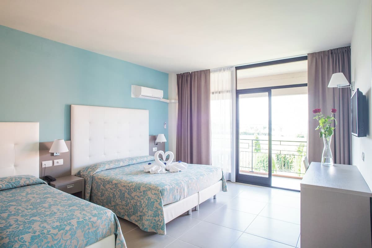 A hotel room with two beds, a TV, a desk, and a balcony with curtains.