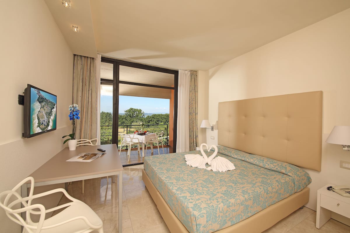 A hotel room with a bed, a desk, and a balcony with a table and chairs.