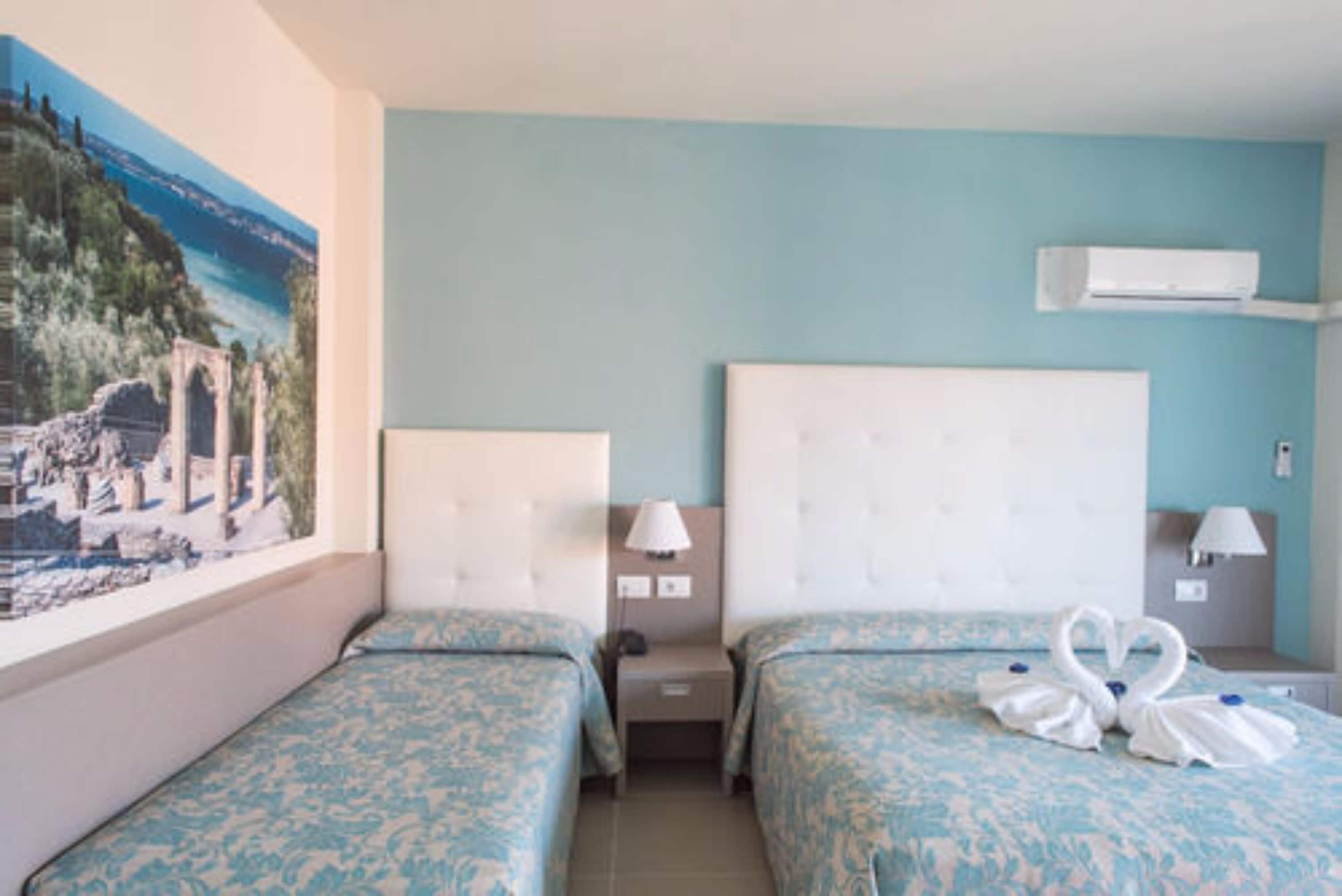 Habitación de hotel con dos camas, un ventanal grande con vistas a ruinas y un equipo de aire acondicionado en la pared.