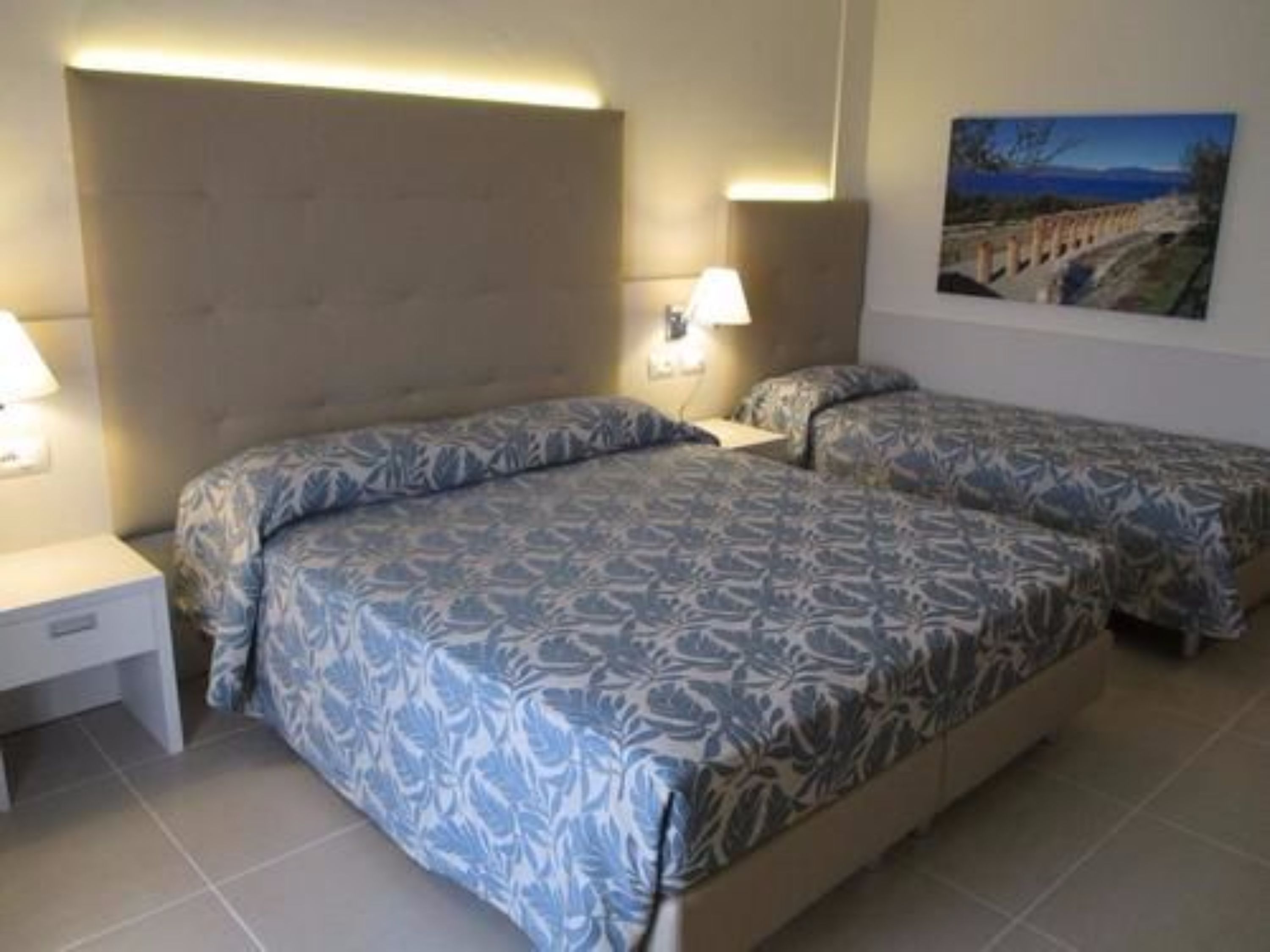 A hotel room with two beds, a nightstand, and a painting on the wall.