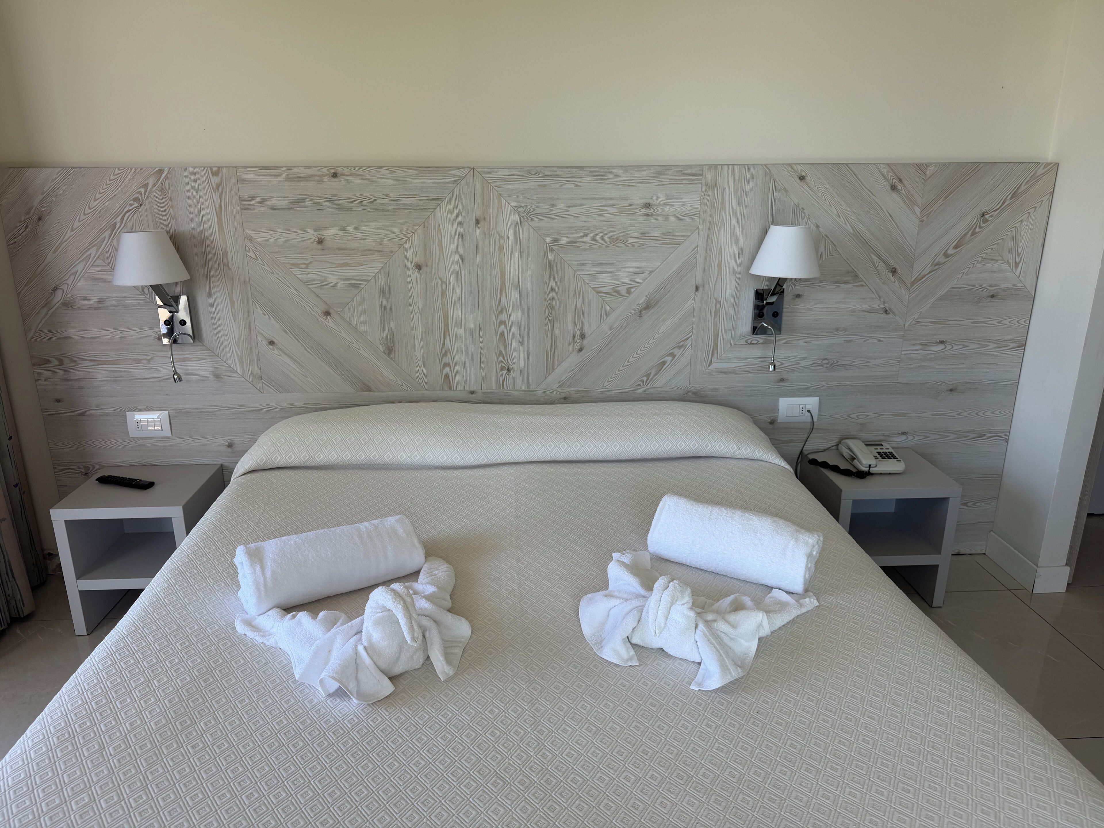Habitación de hotel con una cama grande, dos mesitas de noche, una lámpara de pared y un teléfono sobre una de ellas.
