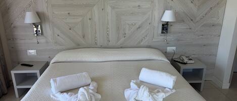 Habitación de hotel con una cama grande, dos mesitas de noche, una lámpara de pared y un teléfono sobre una de ellas.