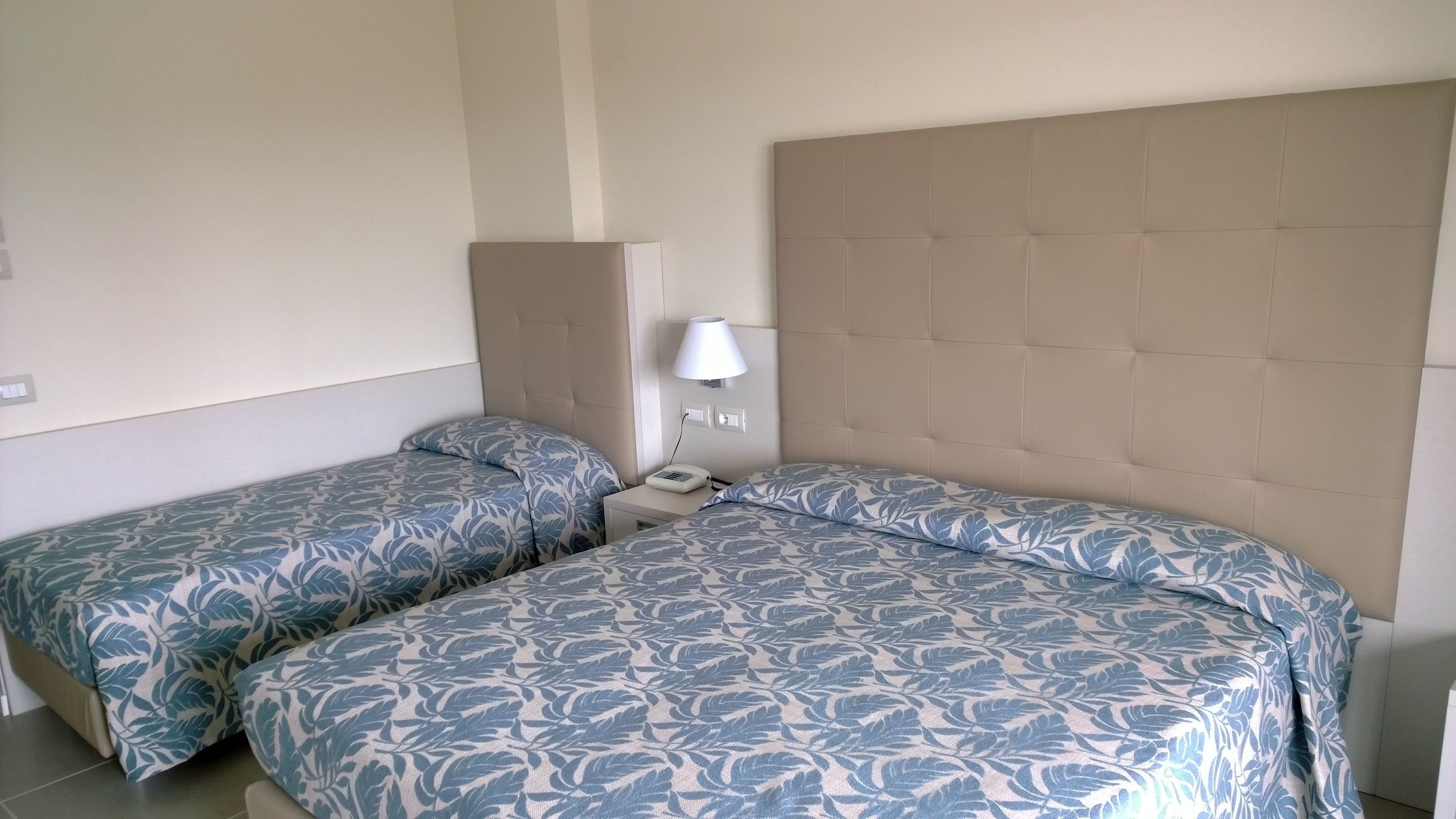Ein Doppelzimmer mit zwei Betten, jeweils mit einem blumengemusterten Überwurf, einem Nachttisch mit Lampe und einem Telefon.
