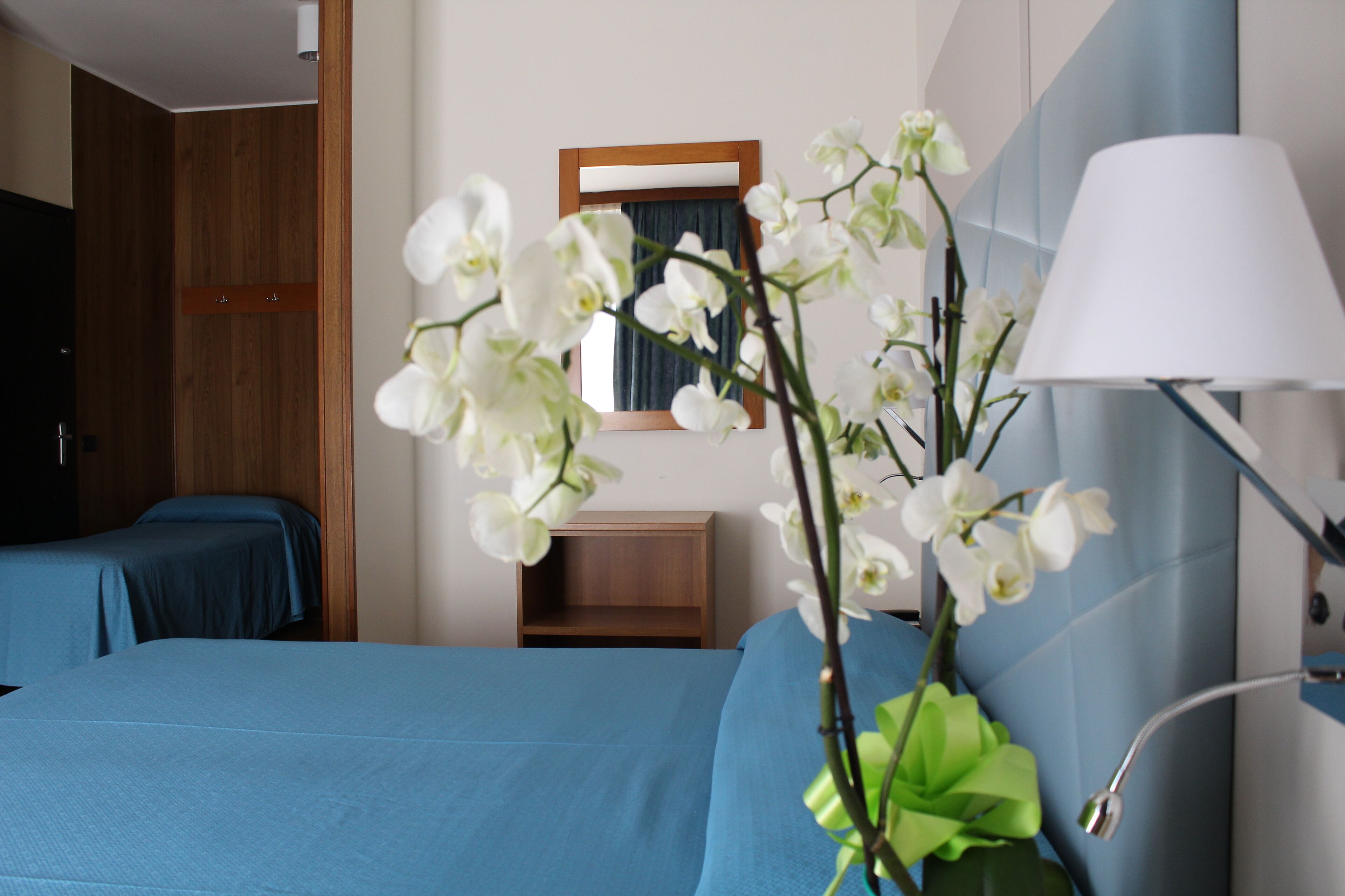 Una camera d'albergo con due letti, un comodino, uno specchio e una lampada.