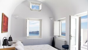 A bedroom with a bed, a window with a view, a small skylight, and a door leading to a balcony.