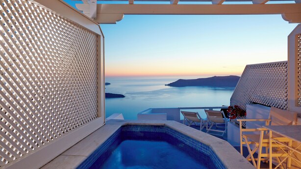 A pool area with a view of the sea and a white pergola structure.