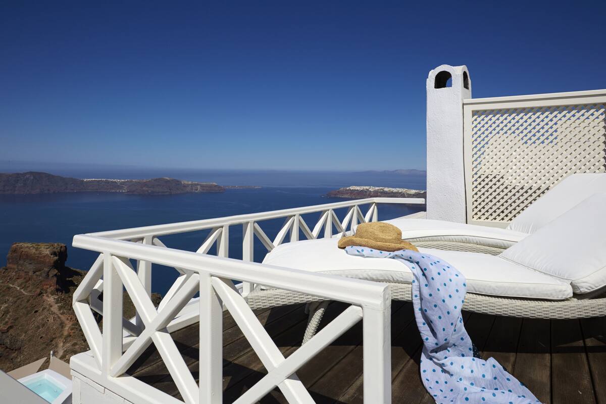 A white wicker lounge chair with a white cushion and a blue polka-dotted towel, overlooking a scenic coastal view.