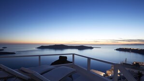 A seaside view from a balcony with lounge chairs, a clear sky, and calm waters.