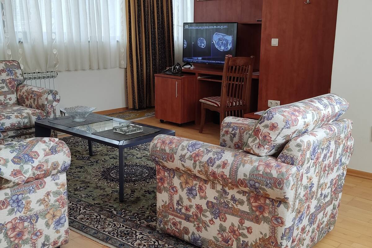 A living room with floral-patterned sofas, a glass coffee table, and a wooden desk with a television.