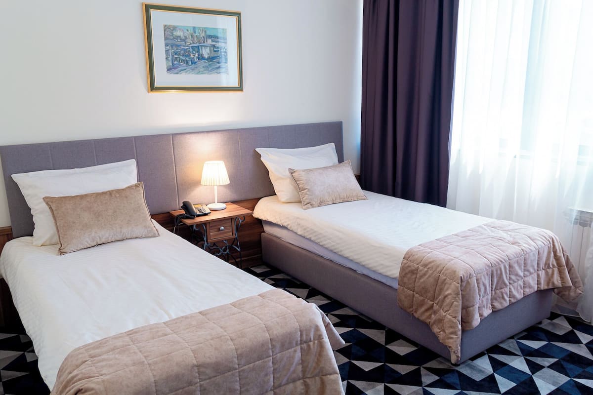 A hotel room with two beds, a nightstand with a lamp, a framed picture on the wall, and a geometric patterned floor.