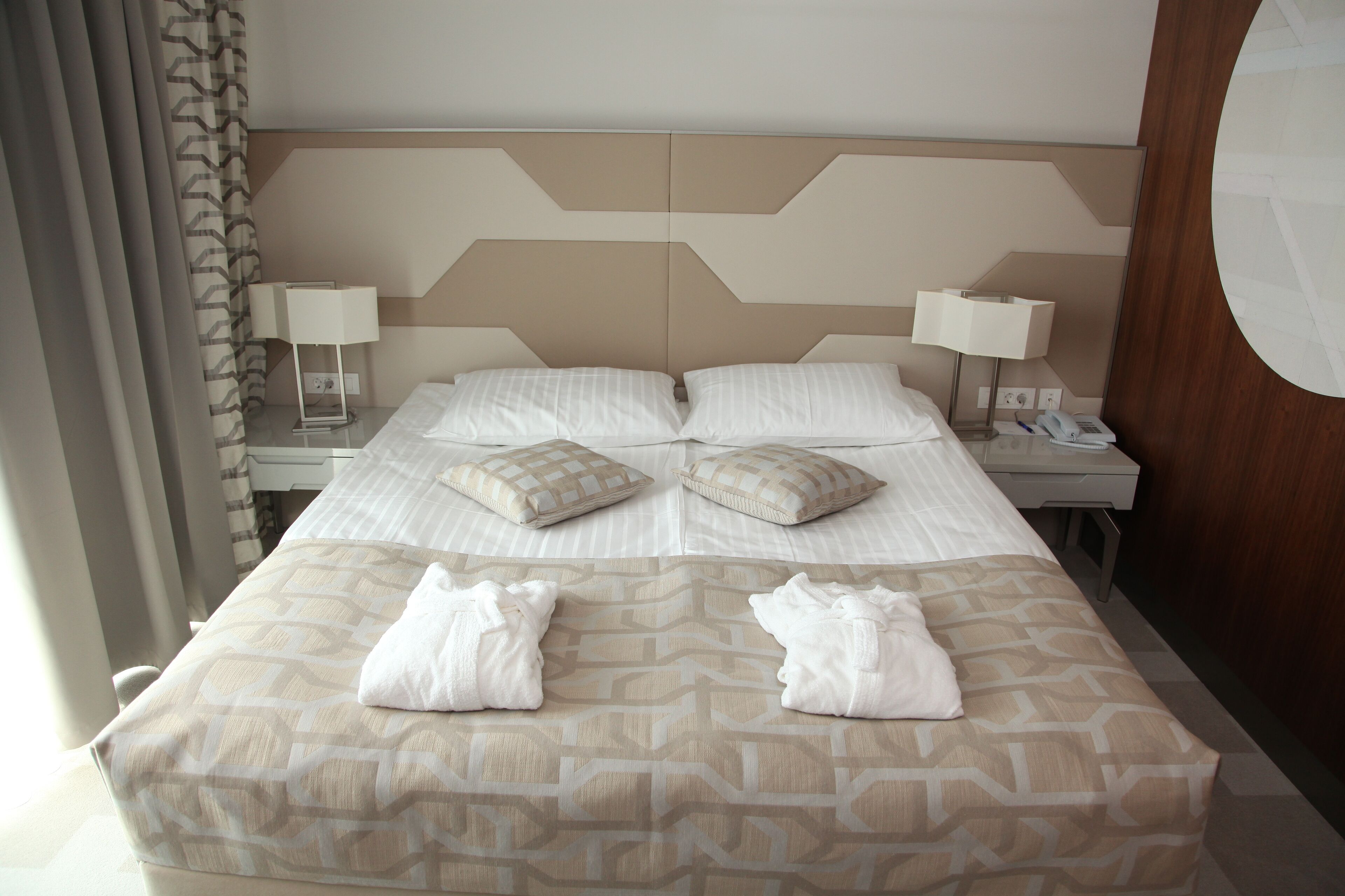 A hotel room with a large bed, two bedside tables with lamps, and a headboard with a geometric pattern.