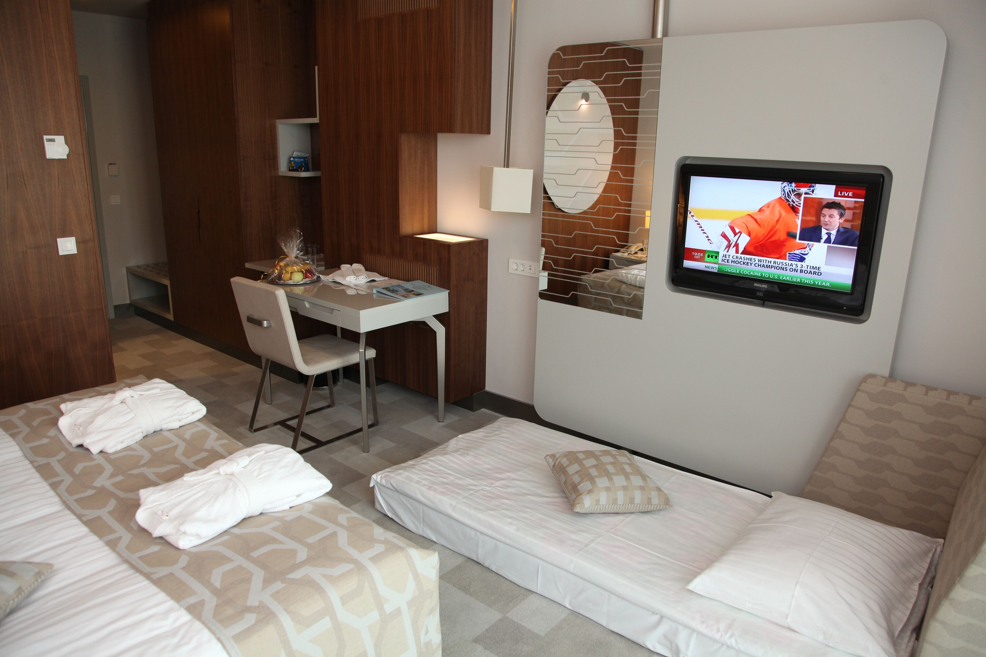 A hotel room with two beds, a desk, a chair, and a TV displaying a sports event.