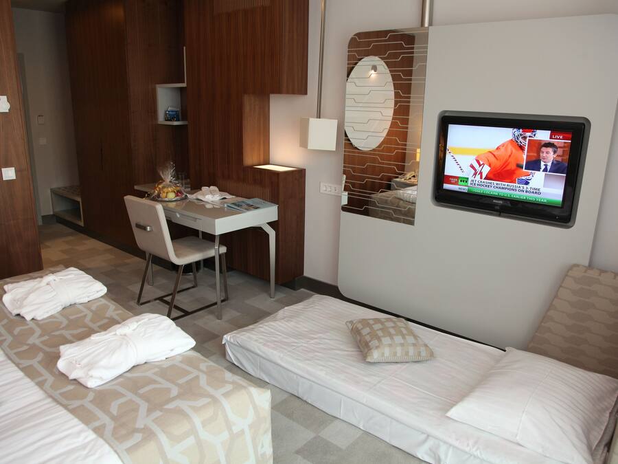 A hotel room with two beds, a desk, a chair, and a TV displaying a sports event.
