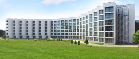 A modern multi-story hotel with a symmetrical facade, large windows, and a central courtyard with greenery.