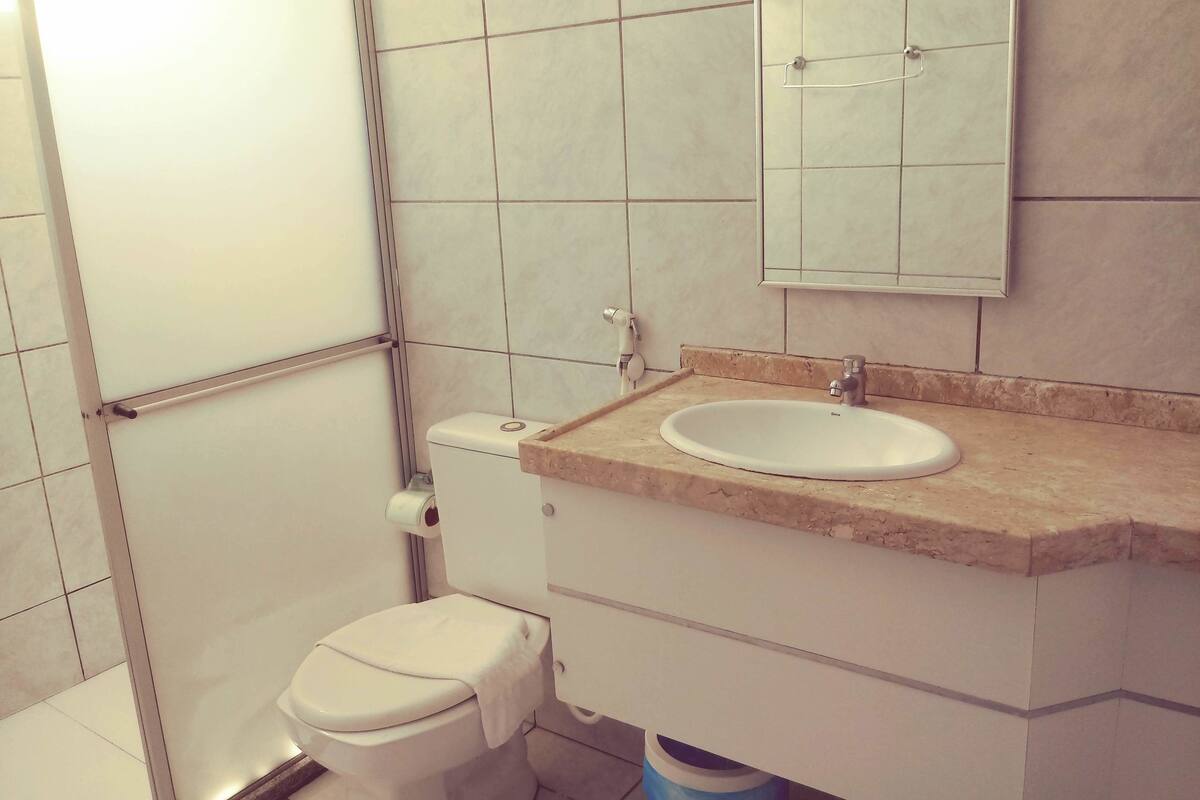 Une salle de bain équipée de toilettes, d’un lavabo, d’un miroir et de murs carrelés.