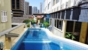 A swimming pool with a tiled edge, surrounded by buildings and a small outdoor seating area with chairs and tables. - Seamar Hotel (Fortaleza)
