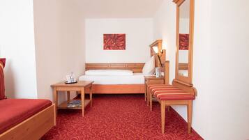 Hotelkamer met een bed, nachtkastje met een lamp, een bankje, een spiegel en een rood karpet met een patroon.