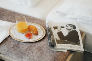 Een ontbijfwagen met jus d'orange, een croissant en een klein kopje thee op een bed, met een tijdschrift.