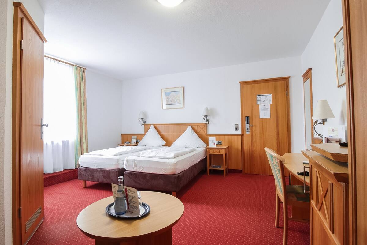 Ein Hotelzimmer mit Bett, Nachttischen, einem Schreibtisch, einem Sessel und einem runden Tisch mit Speisekarte.