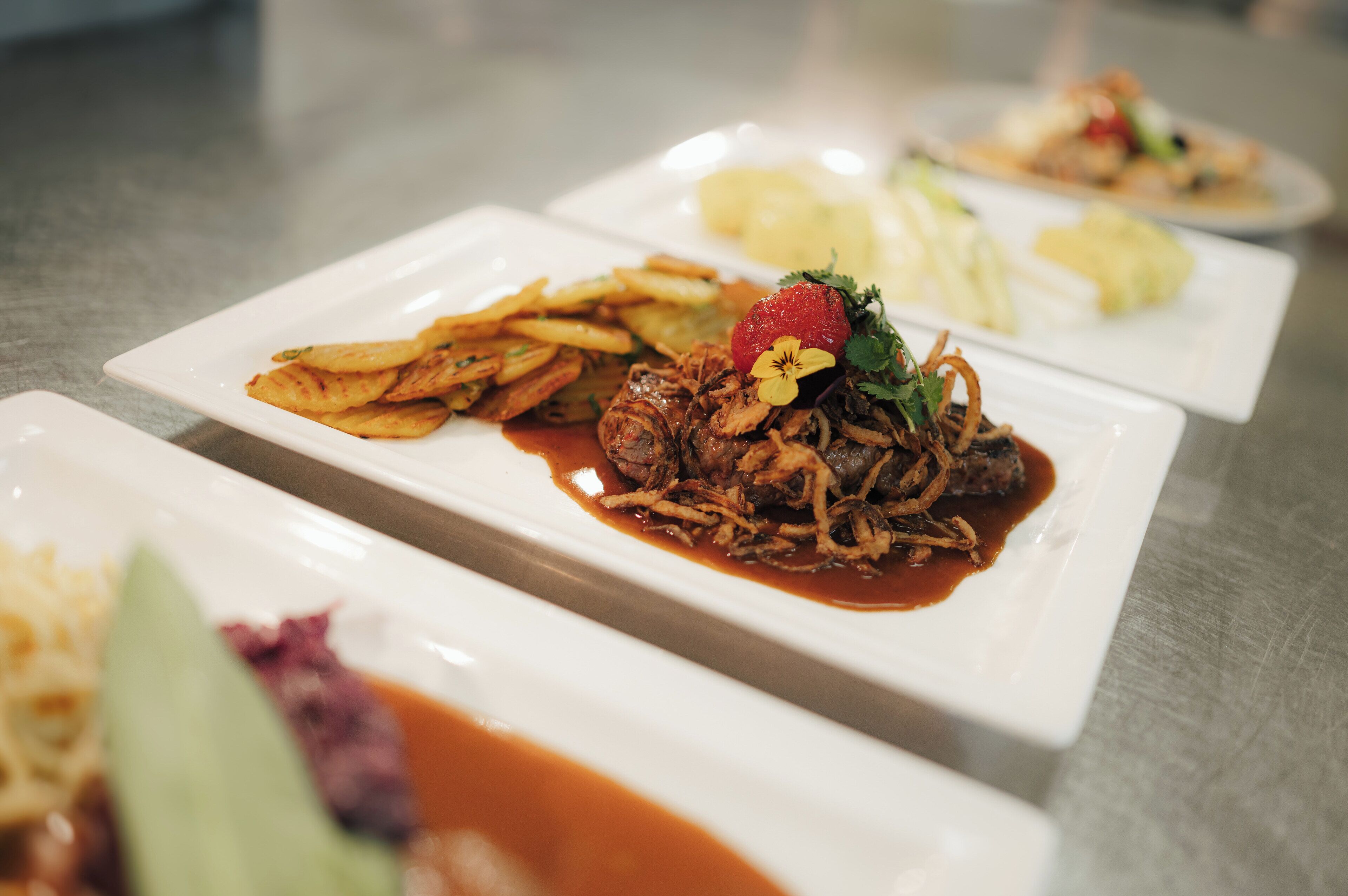 Een restauranttafel met meerdere vierkante witte borden eten erop.